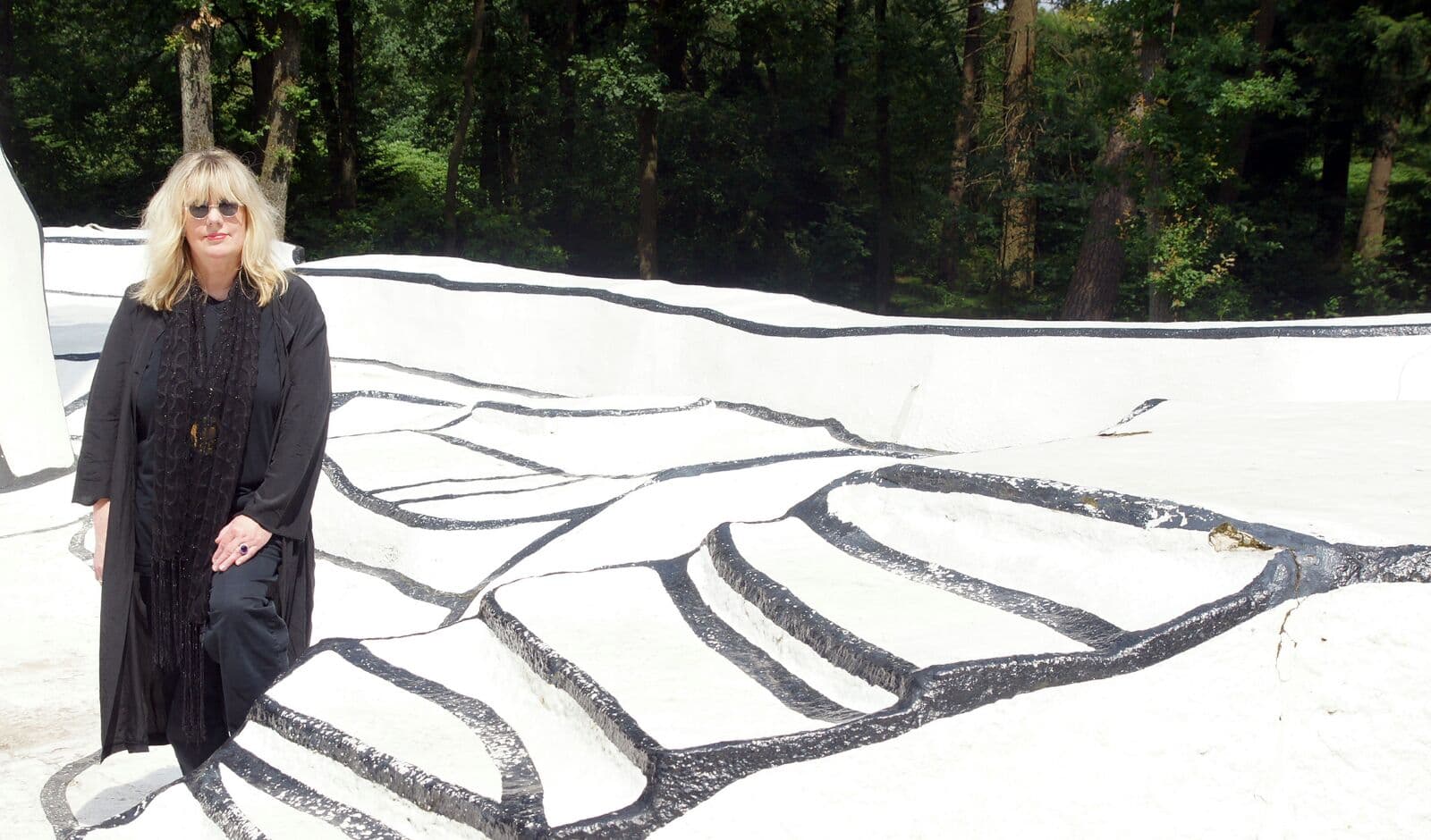 Jutta van den Berg in einer weissen Land-Art-Installation mit breiten schwarzen Linien, ganz in Schwarz gekleidet